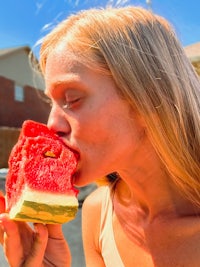 a woman is eating a slice of watermelon